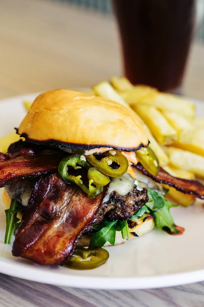 Close-up of a gourmet burger with cheese, bacon, jalapeños, and fries.