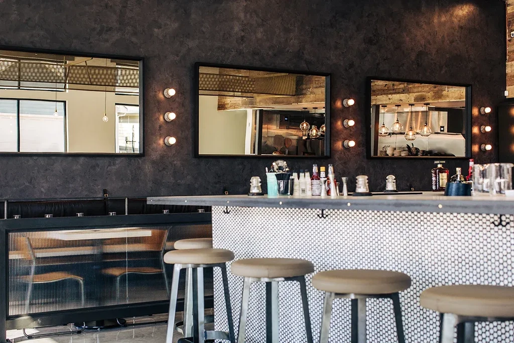 Sophisticated modern bar with dark walls, tiled counter, and vanity mirrors.