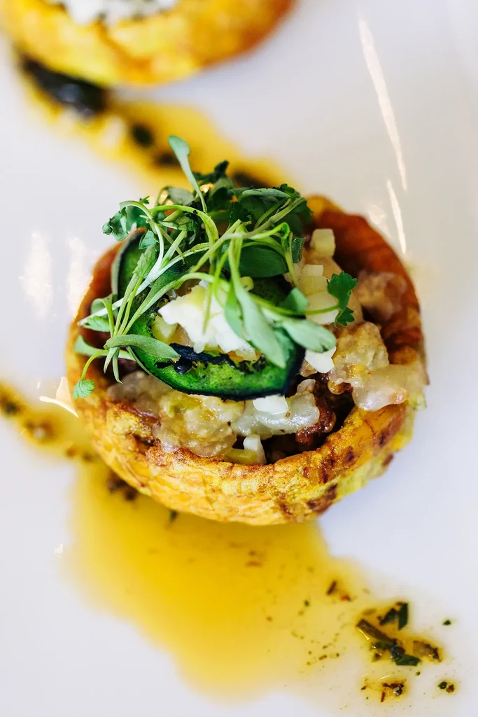 Golden tostones cup appetizer with savory filling, microgreens, pepper, and sauce.