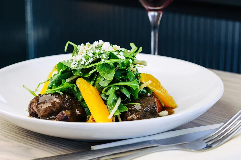 Plate of arugula salad with cheese, meat, and orange segments.