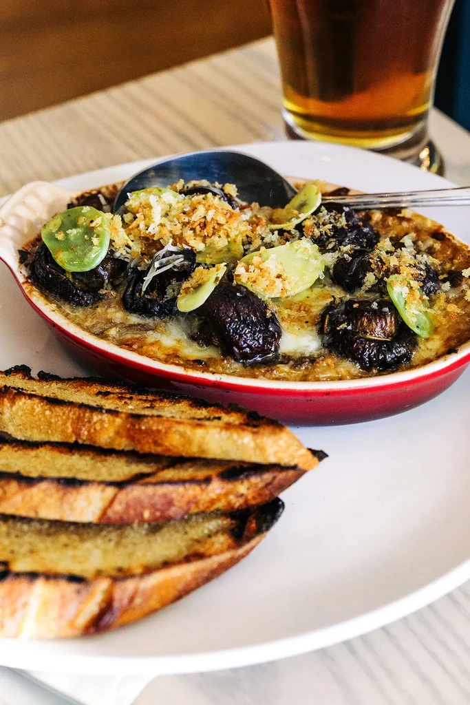 Close-up of a savory baked dish, grilled bread, and beer.