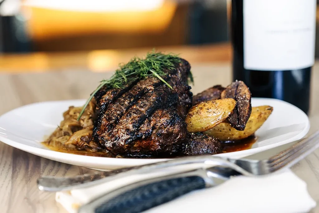 Grilled steak with herbs, roasted potatoes, dark sauce; dining setting.