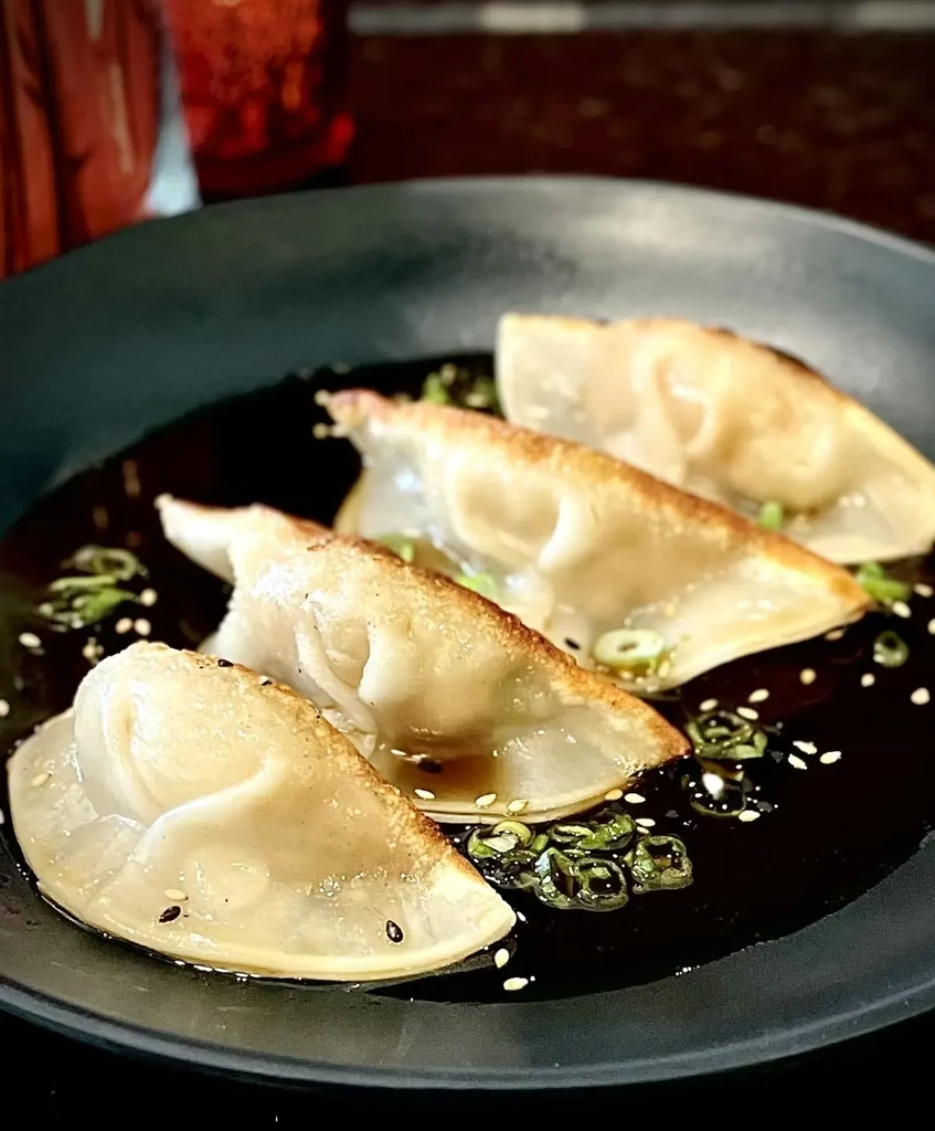 Four pan-fried gyoza in sauce, garnished with green onions and sesame.