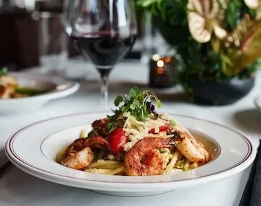 Close-up of shrimp pasta with tomatoes, cheese, and microgreens.