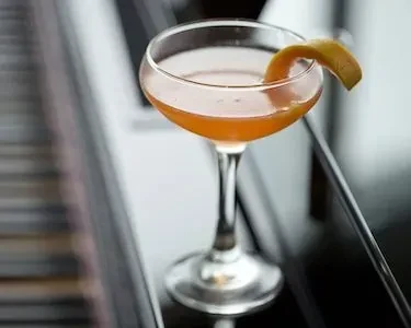 Amber cocktail in coupe glass with citrus peel on dark surface.