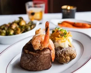 Close-up of steak, shrimp, and loaded baked potato on white plate.