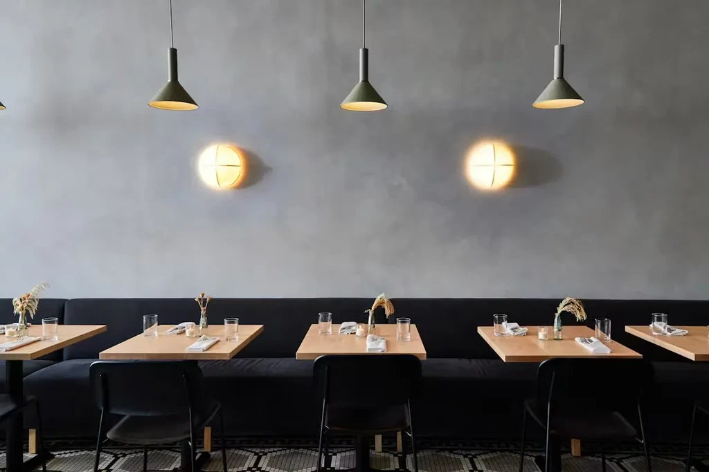 Modern restaurant interior: bench seating, square wooden tables, geometric tile floor.