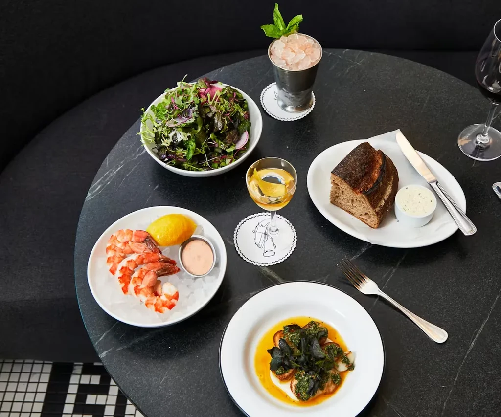 Overhead view of a dark restaurant table with diverse dishes and drinks.