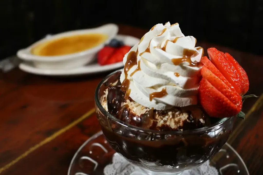 Chocolate dessert with whipped cream, caramel, strawberries; blurred crème brûlée.