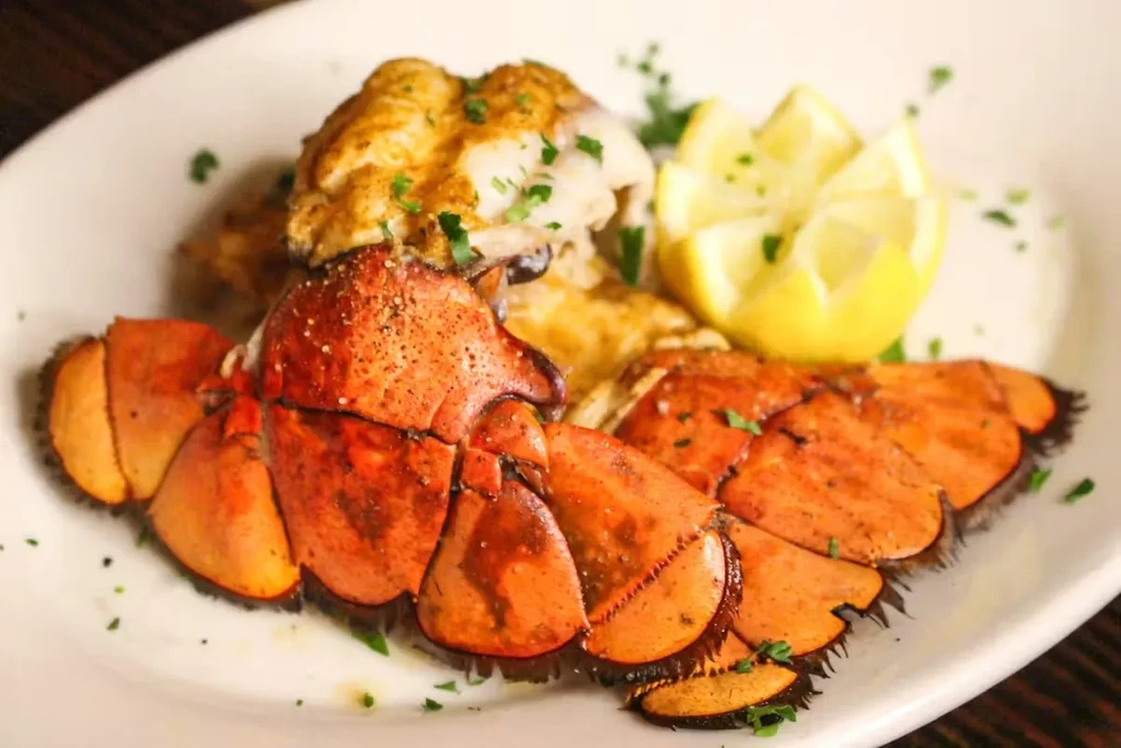 Cooked orange lobster tails, fish, lemon, and herbs on a white plate.