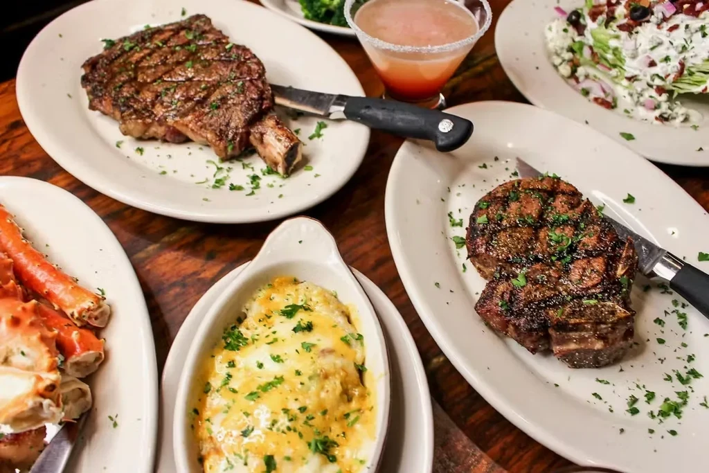 Overhead view of an abundant meal with steak, crab, gratin, and cocktail.
