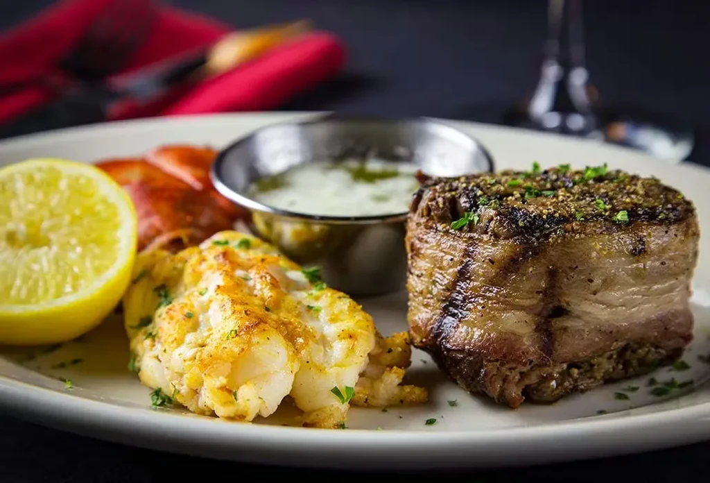 Grilled surf and turf: bacon-wrapped steak, lobster, and lemon.