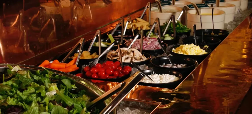 Well-stocked salad bar with colorful fresh ingredients, dressings, and serving tongs.