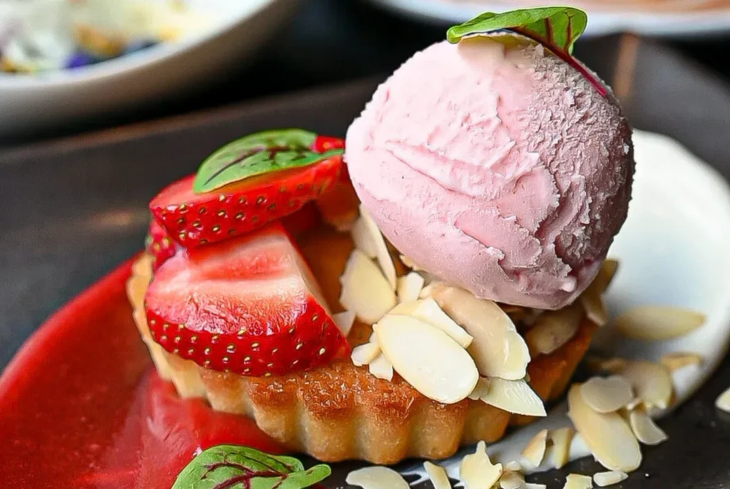 Golden-brown strawberry tart with pink ice cream, almonds, and green leaves.
