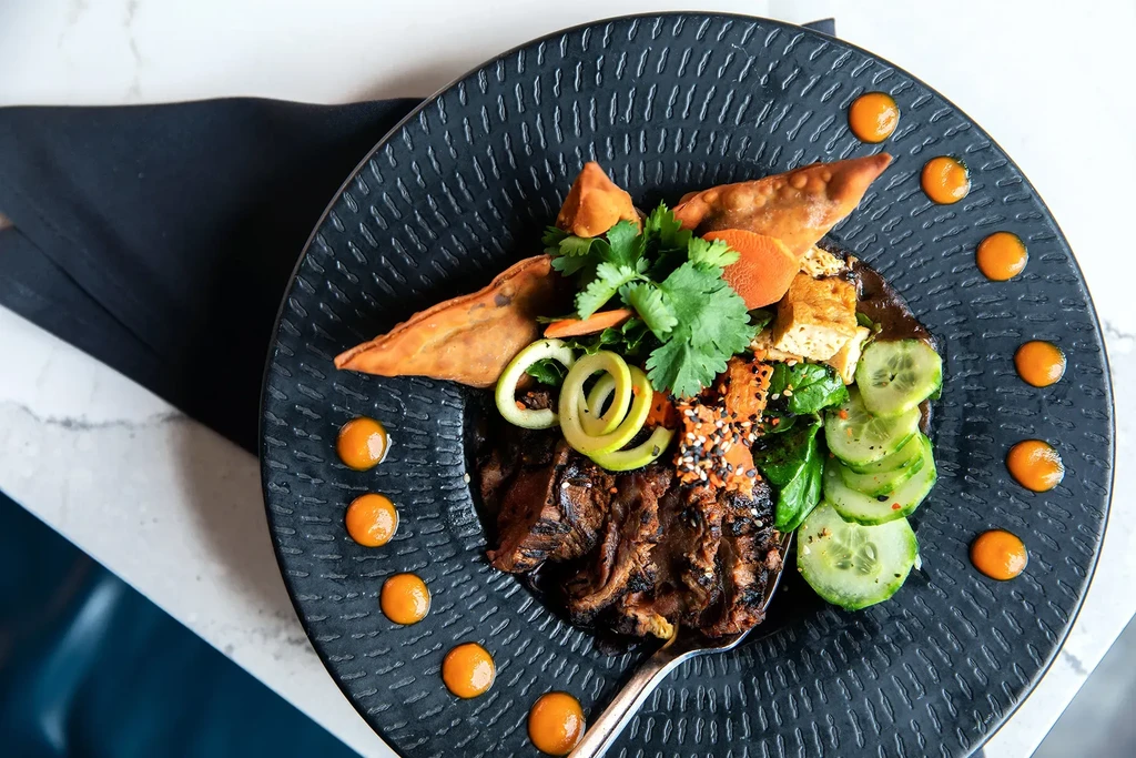 Expertly plated Asian meal with grilled meat, fresh vegetables, and dumplings.