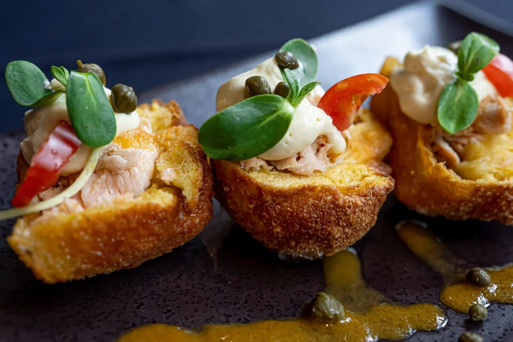 Three shredded meat appetizers in bread cups, garnished on a dark plate.