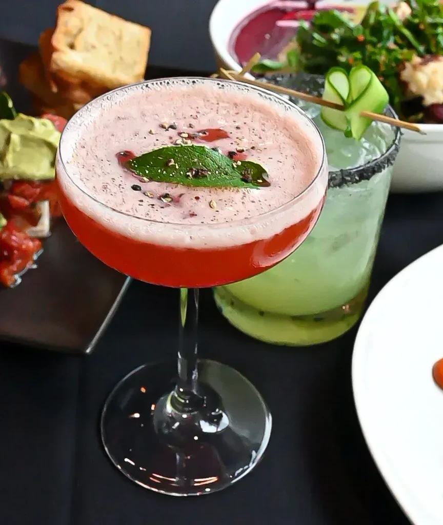 Red and green cocktails with appetizers on a dark table.