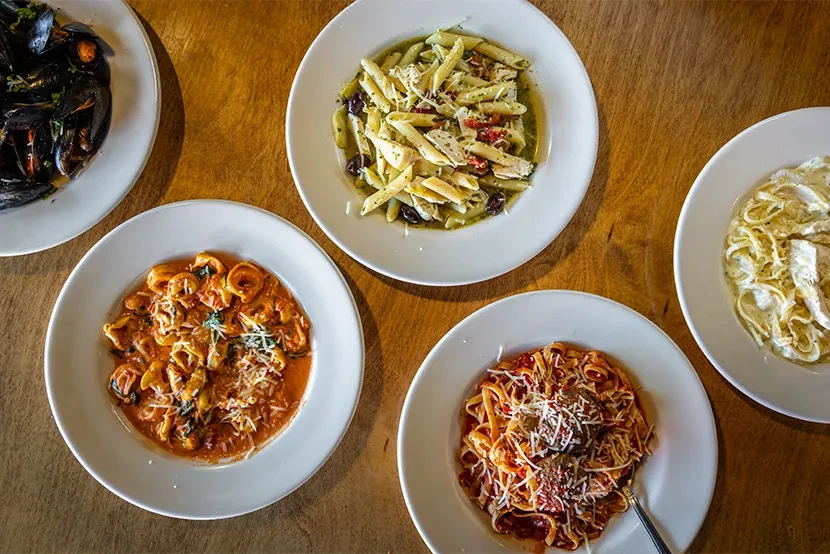 Overhead shot of five different pasta and mussel dishes.