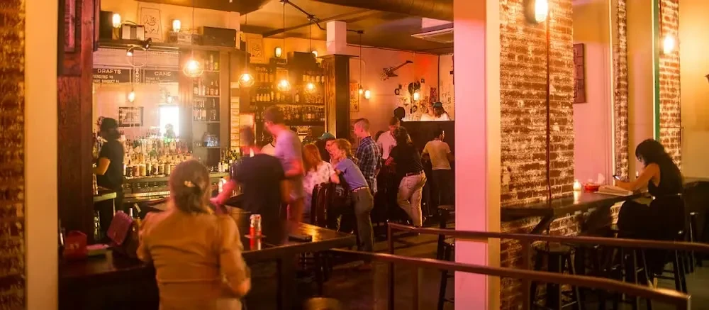 Lively bar interior with warm lighting, brick walls, and patrons.