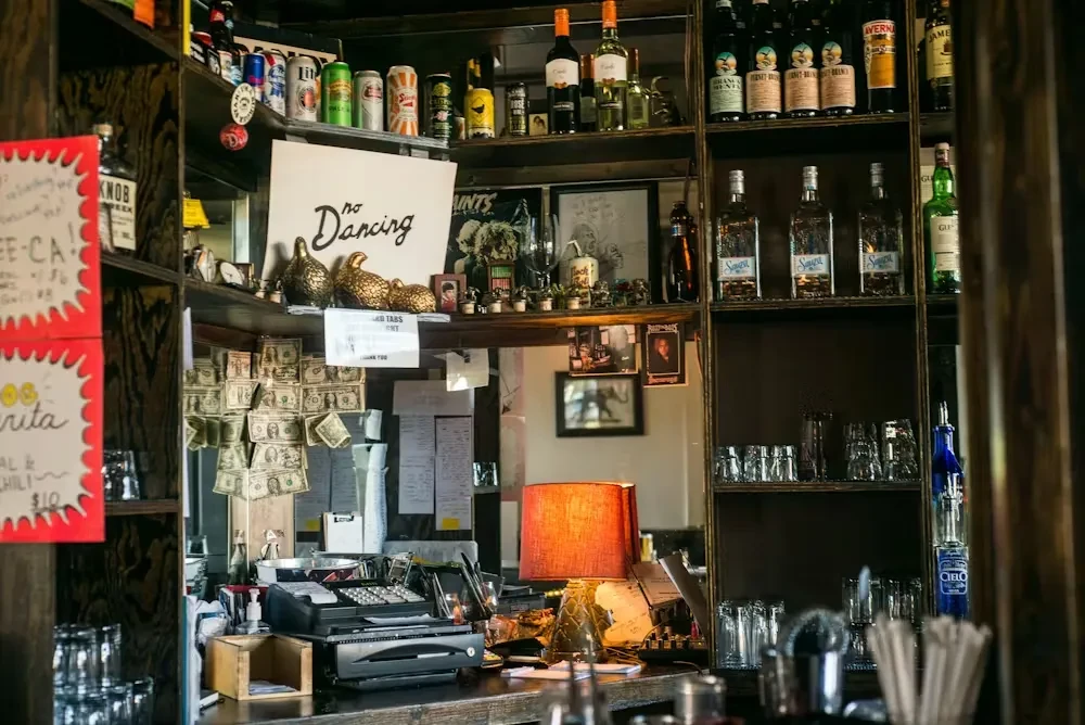 A detailed, eclectic bar counter stocked with drinks and quirky decor.
