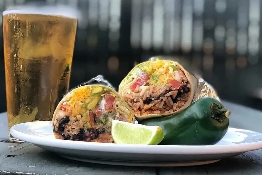 Cut burrito showing fillings, lime, jalapeño, and cold amber drink.