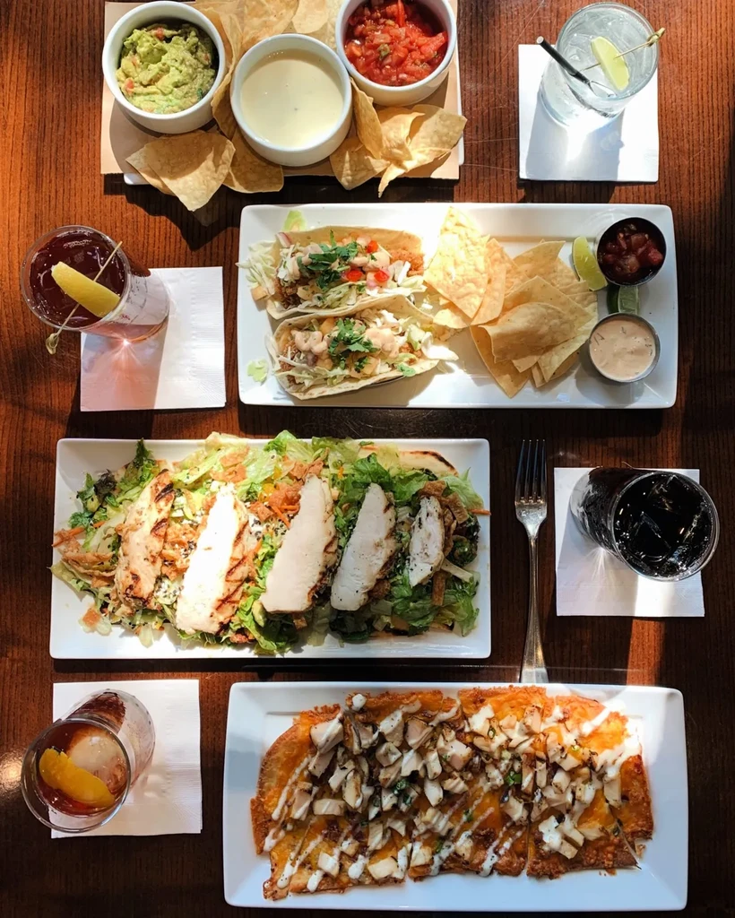 Wooden table laden with tacos, salad, dips, and assorted beverages.