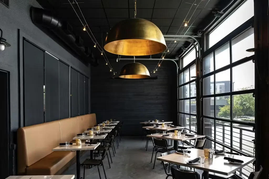 Industrial restaurant interior: dark walls, tan booth, brass lights, urban windows.