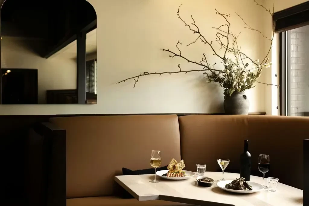 Elegant restaurant table with food, drinks, leather booth, and arched mirror.