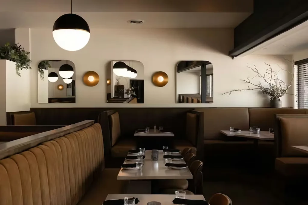Empty modern restaurant interior with tan booths, set tables, and pendant lights.