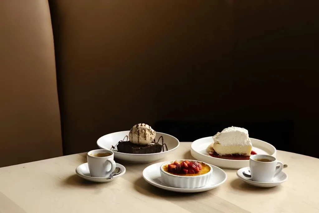 Table with creme brulee, chocolate cake, cheesecake, and espresso cups.