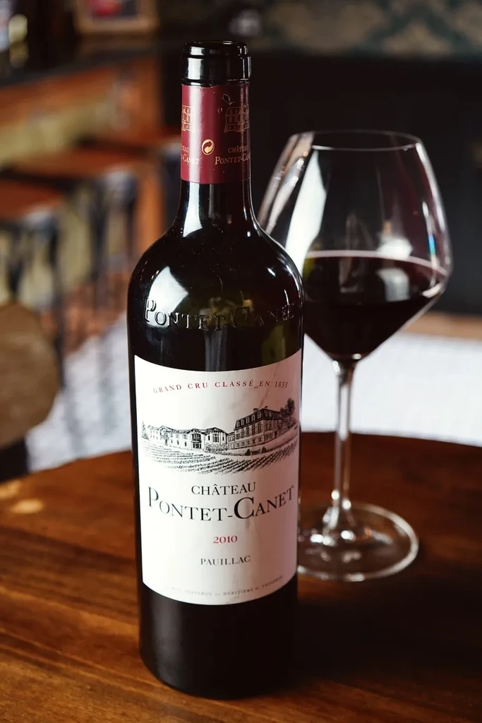 Château Pontet-Canet 2010 red wine bottle and glass on dark wood.
