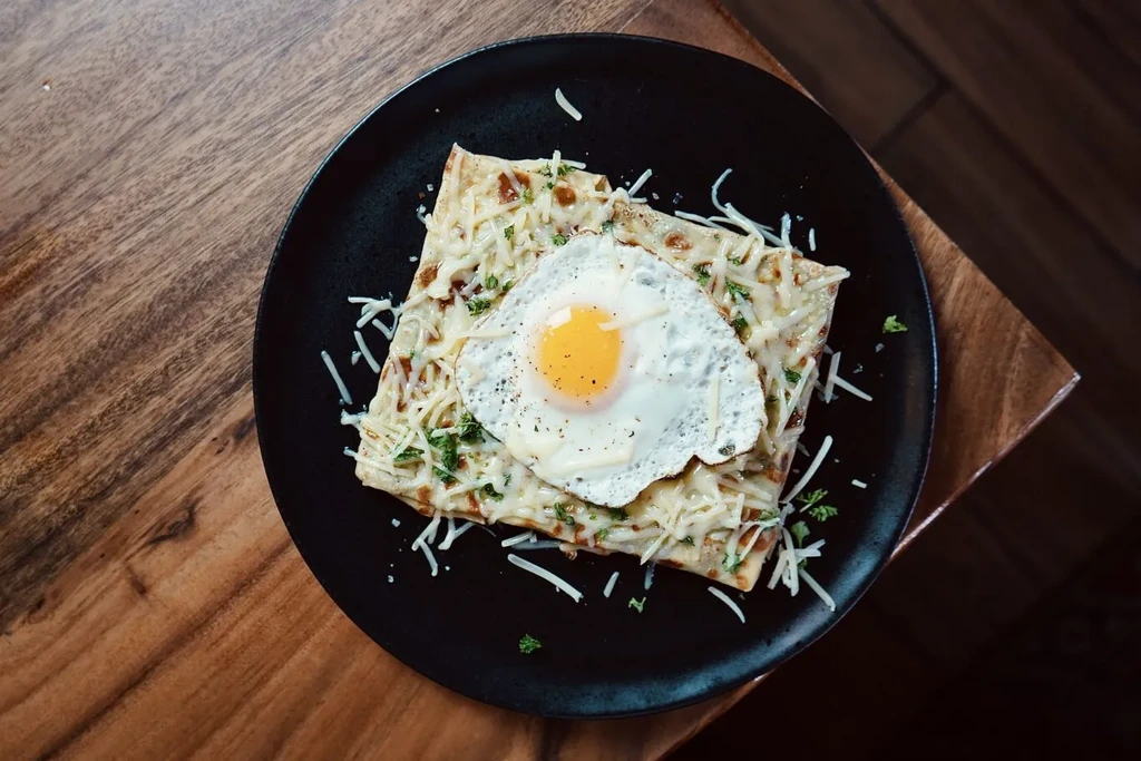 Melted cheese crepe topped with a sunny-side-up egg and fresh herbs.