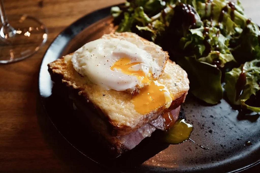 Grilled sandwich with runny fried egg and green salad on dark plate.