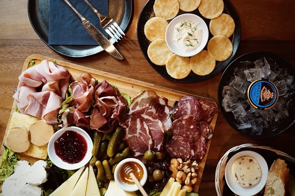 Overhead view: large charcuterie board, caviar tin, crackers, and baguette.
