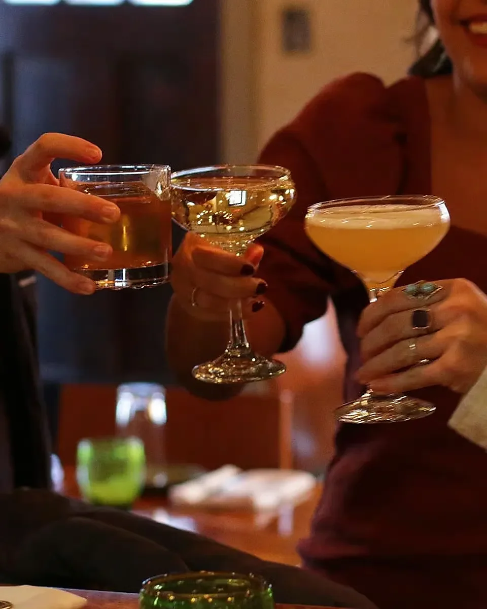 Guests toasting with coupe cocktails and a whiskey glass at bar