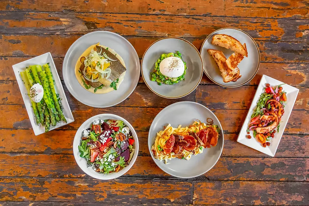 Overhead spread of plated dishes including asparagus, salad, pasta and octopus