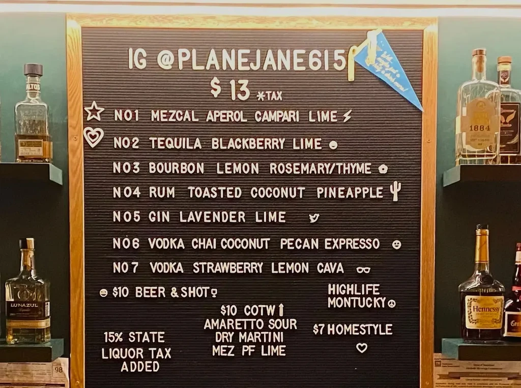Cocktail menu on a felt letter board, surrounded by liquor bottles.