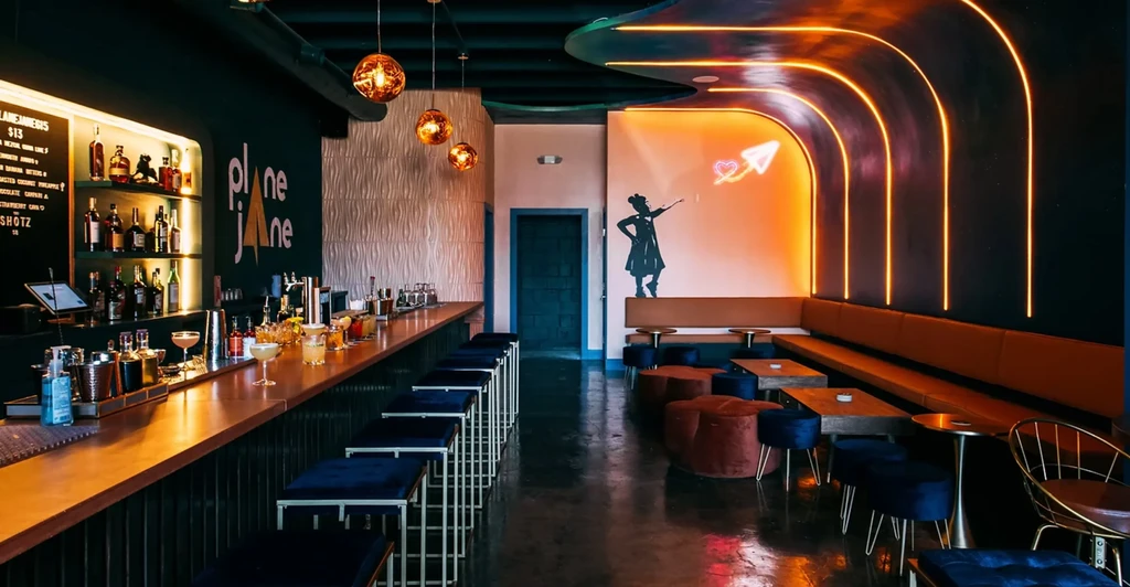 Modern bar interior "plane jane" with wooden bar, neon lights, and mural.