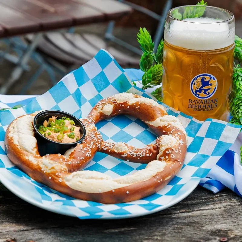 Salted pretzel, creamy dip, and Bavarian beer on a biergarten table.