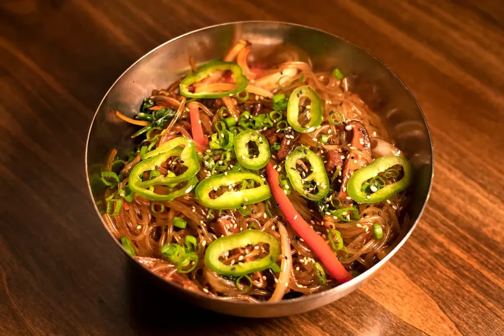 Japchae noodles with peppers, sesame, and colorful vegetables in a bowl.