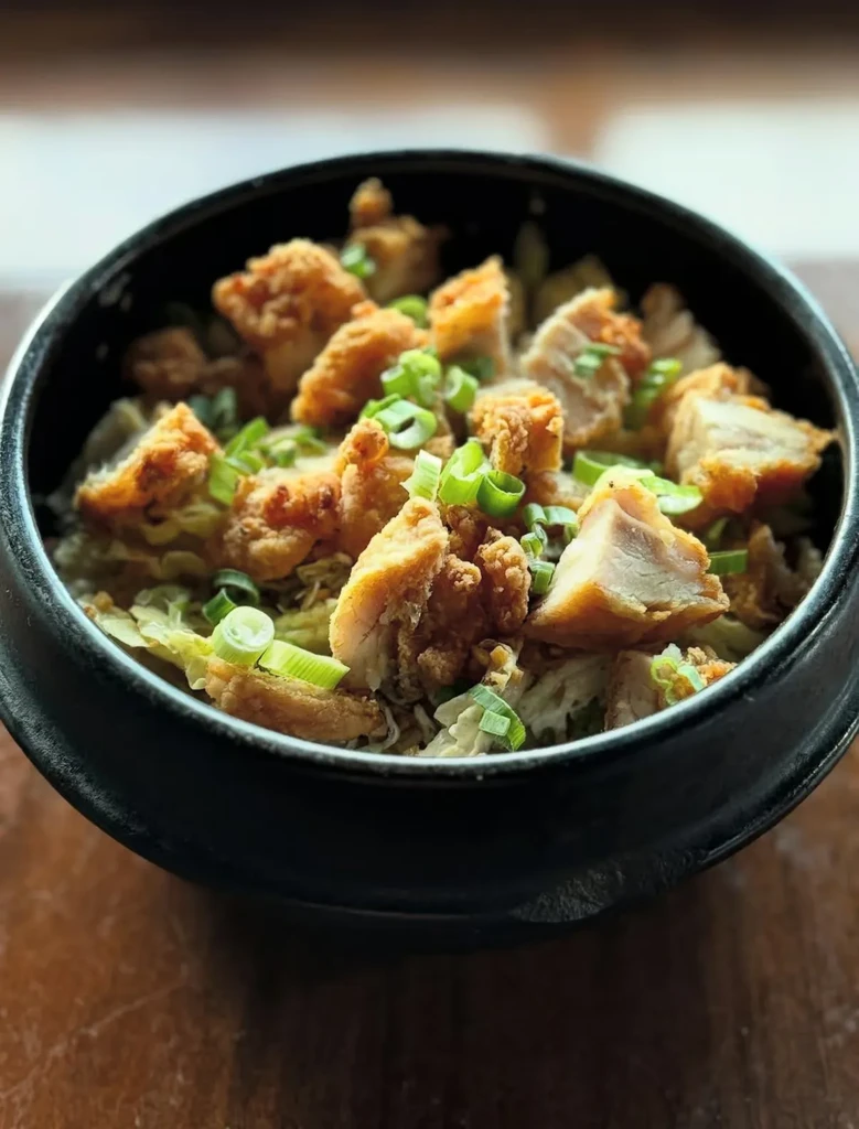 Crispy golden-brown fried chicken, green onions, shredded greens in a dark bowl.