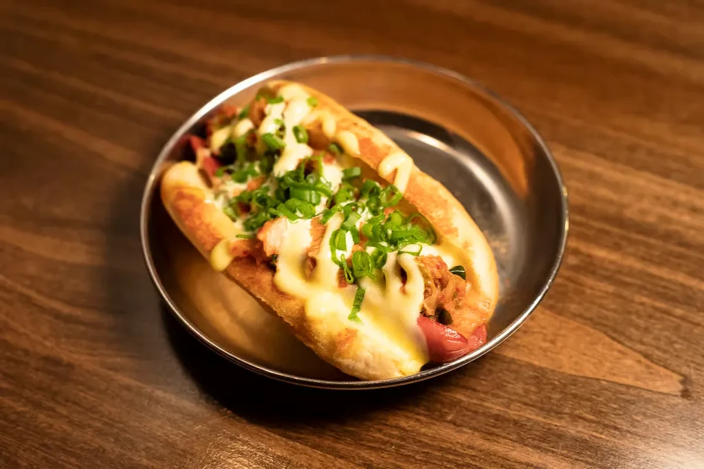 Close-up hot dog with cheese sauce, chili, and green onions.