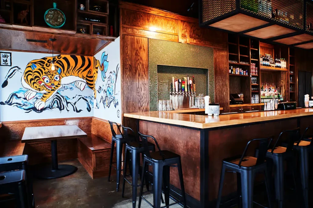 Restaurant interior with a long bar, tiger mural, and dining booth.