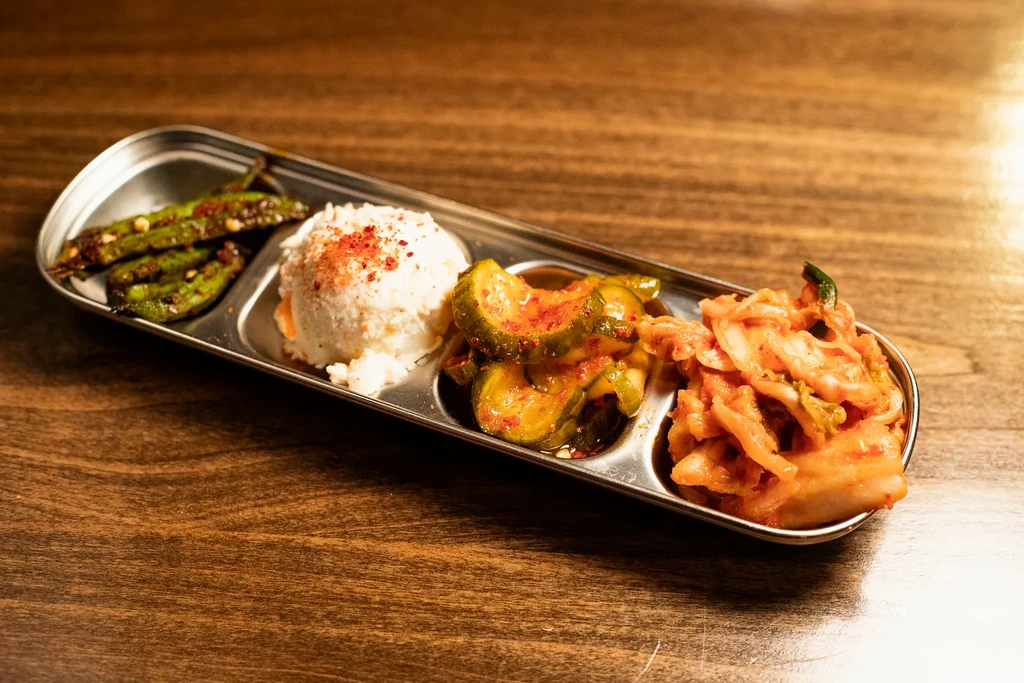 Stainless steel tray with chili peppers, white purée, pickled cucumbers, kimchi.