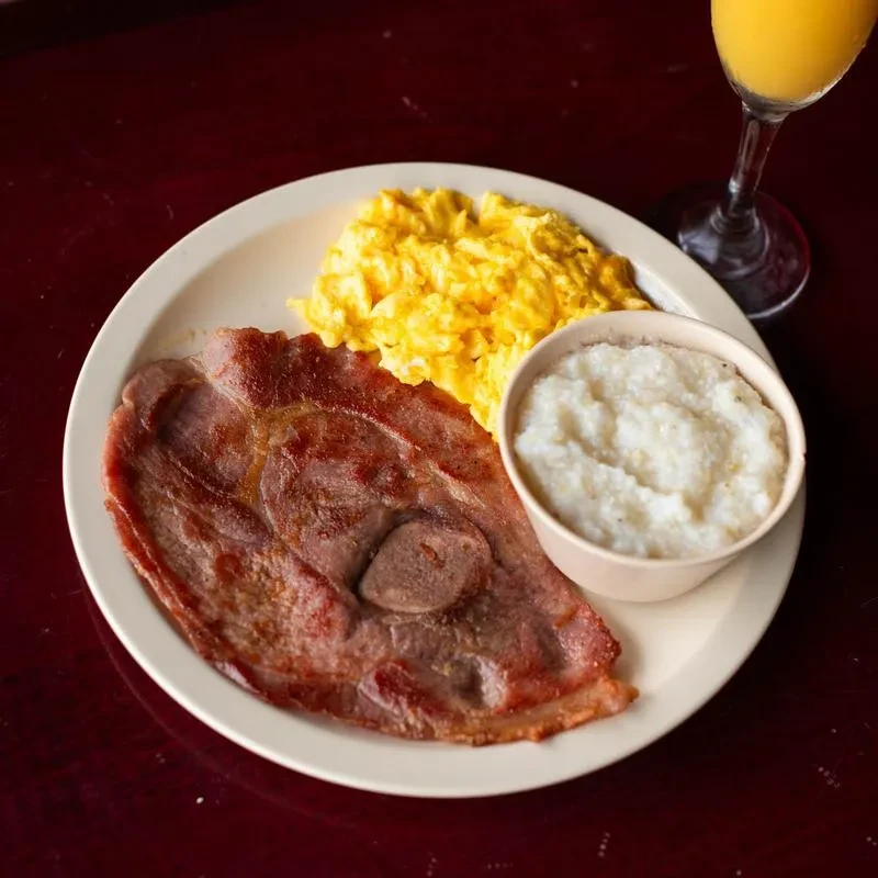 Breakfast plate with seared ham, fluffy eggs, creamy grits, orange juice.