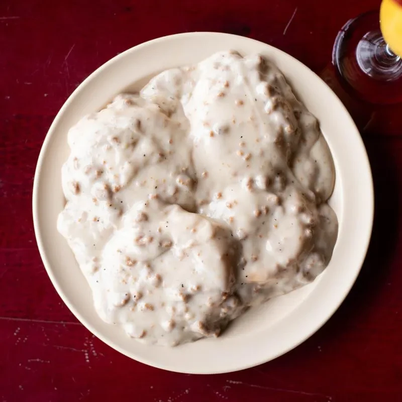Biscuits and sausage gravy on an oval plate with a drink.