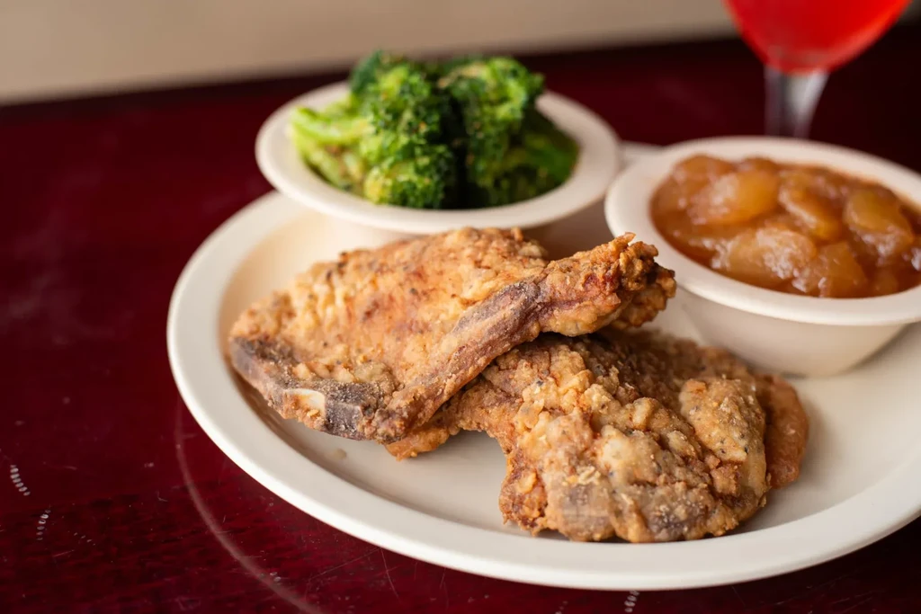Two fried chops/chicken, steamed broccoli, stewed apples, and a red drink.