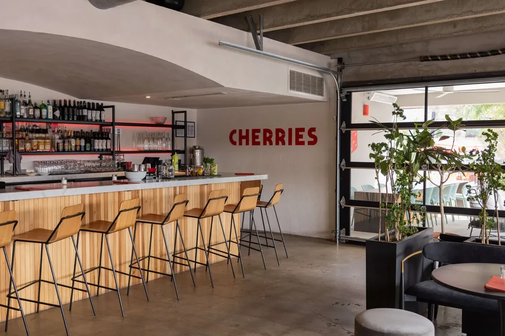 Modern bar interior with wooden counter, stocked liquor shelves, and CHERRIES sign.