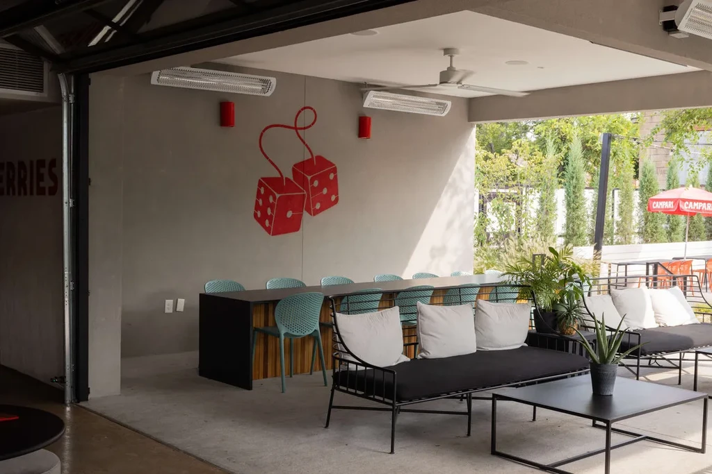 Modern restaurant patio featuring communal table, lounge sofas, and red dice mural.