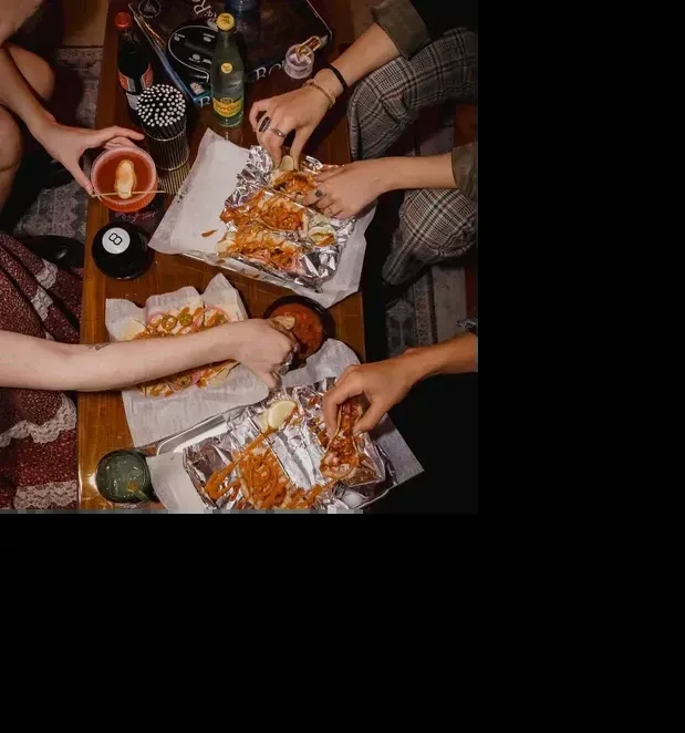 Overhead view: hands sharing tacos, drinks, and salsa on a table.